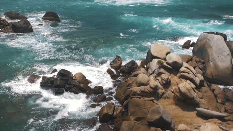 Waves-crashing-against-a-stack-of-rocks-on-a-cliff-in-slow-motion-in-Tayrona-Park,-Colombia
