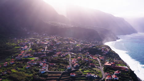 Aerial-view-with-sun-lens-flare-behind-mountains-and-beautiful-old-village-of-Ponta-Delgada-beside-Atlantic-Ocean
