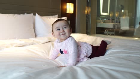 Super-happy-infant-baby-girl-dancing-on-a-white-bed-Hotel-room,-shaking-head-and-excited-the-crawling-dance