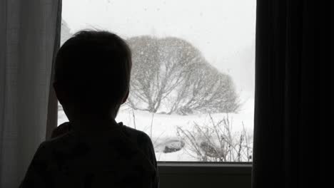 Silhouette-of-sad-young-boy-locked-inside-yearning-to-play-outside,-looking-through-window-during-covid-19-lockdown