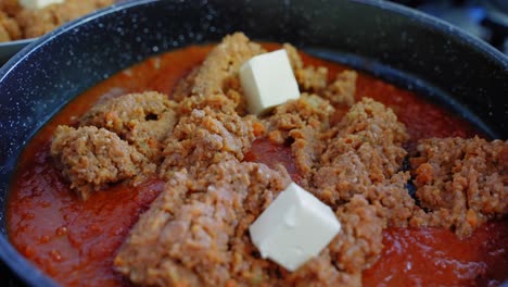 Close-up-of-adding-cubes-of-butter-to-a-pan-of-Bolognese-tomato-sauce-while-cooking
