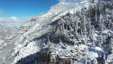 Sonnige-Winterlandschaft,-Drohnenluftaufnahme-Von-Schneebedeckten-Berghügeln,-Gipfeln,-Wolken-Und-Nadelwald