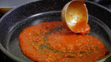 Slow-motion-close-up-of-a-ladle-of-tomato-sauce-being-added-to-a-frying-pan