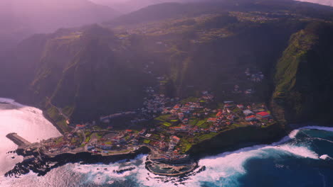 Filmische-Luftaufnahme-Von-Porto-Moniz,-Umgeben-Von-Hohen-Bergen-Und-Blauem-Atlantik-Während-Des-Sonnenuntergangs