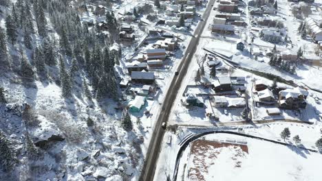 Birdseye-aerial-view-of-winter-traffic-on-countryside-road-by-Ouray-Colorado-USA-and-snow-capped-landscape-on-sunny-day,-top-down-drone-shot