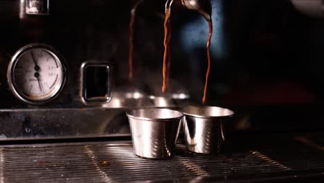 Slow-motion-view-of-espresso-dripping-from-machine-to-fill-two-silver-cups-on-grate