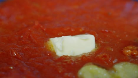 Close-up-of-butter-melting-into-a-red-tomato-sauce