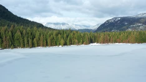 Aerial-Ascending-View-of-Frozen-Lake-with-Vast-Forest-and-Mountain-Landscape