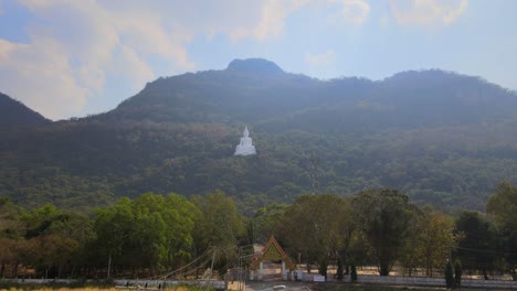 Luang-Por-Khao,-Wat-Theppitak-Punnaram,-descending-aerial-footage-of-the-famous-white-temple-on-the-mountain-revealing-the-arch-gate,-street-lights,-road-going-inside,-landscape-as-a-whole