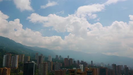 Aerial,-Drone-Flies-Over-Top-of-Apartment-Buildings,-Reveals-Medellin-Skyline-in-Distance,-Blue-Sky