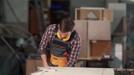 An-attractive-man-in-a-working-uniform-removes-the-clamp-and-blows-dust-from-a-wooden-product