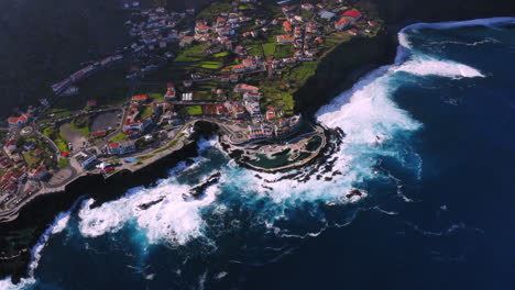 Absteigende-Luftaufnahme-Von-Porto-Moniz-Mit-Natürlichem-Pool-Und-Krachenden-Wellen-An-Der-Küste-Bei-Sonnigem-Tag