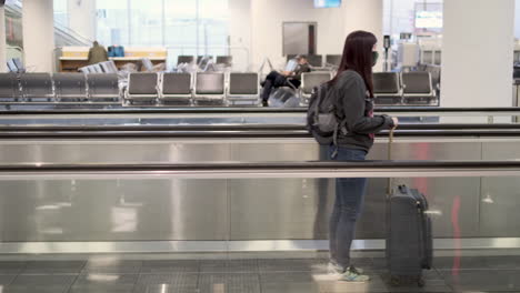 Side-shot-of-a-young-woman-wearing-mask-rideing-moving-walkway-with-suitcase