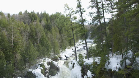 River-flows-through-a-frozen-winter-forest-landscape-into-a-waterfall