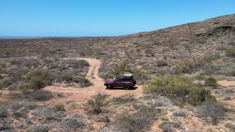 Aerial-track-shot-of-4x4-safari-vehicle-driving-on-hilly-desert-during-sunlight