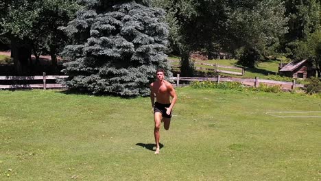 Young-caucasian-fit-attractive-male-sprinter-running-exercising-outdoors-with-green-vegetation-background-slow-motion-aerial