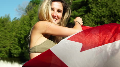Una-Mujer-Joven-Y-Segura-De-Sí-Misma-En-Bikini-Ondea-Una-Bandera-Canadiense-A-La-Cámara-Mientras-Posa-En-Un-Río