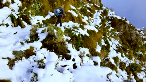 Back-view-of-solo-woman-trekker,-hiking-the-snowy-steep-mountainous-terrain-of-Routeburn-track
