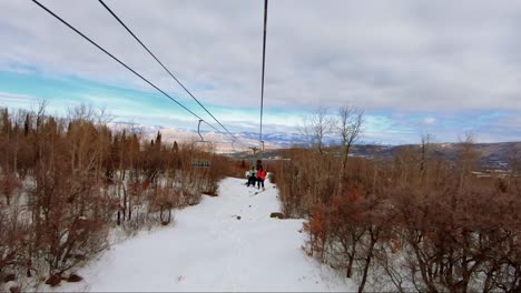 Beautiful-point-of-view-from-a-ski-lift-at-a-ski-resort-in-Colorado-on-an-overcast-winter-day-with-tall-aspen-and-pine-trees-with-stunning-desert-orange-and-red-colored-landscape-in-the-background