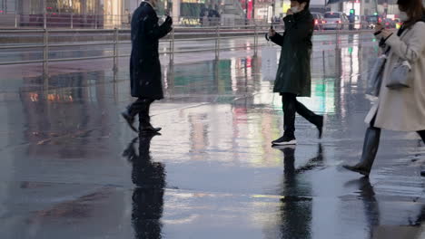 Modische-Leute-In-Maske,-Die-Während-Des-Schneefallabends-In-Tokio,-Japan,-Auf-Nasser-Straße-Mit-Regenschirm-Spazieren-Gehen