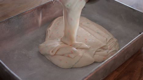 Funfetti-cake-batter-being-poured-into-a-flour-lined-metal-cake-pan-in-4k-60fps