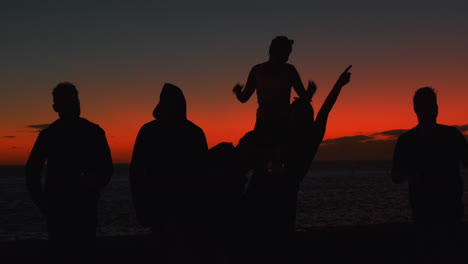 Dark-Silhouette-showing-group-of-young-people-celebrating-outdoors-and-enjoying-red-colored-sunset-in-background