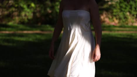 woman-with-a-white-strapless-summer-dress-walk-slowly-outdoors-from-the-shadow-into-the-sun-opening-her-arm-in-a-revealing-movement