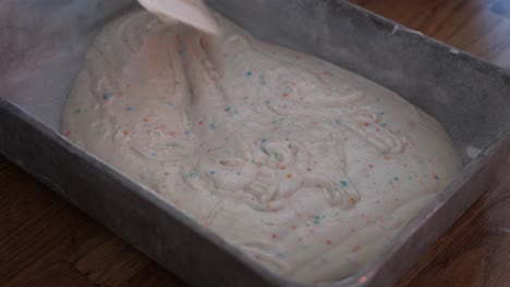Spreading-out-and-evening-white-funfetti-cake-batter-or-frosting-with-rainbow-sprinkles-using-a-rubber-spatula-and-spinning-the-pan,-in-4k-60fps