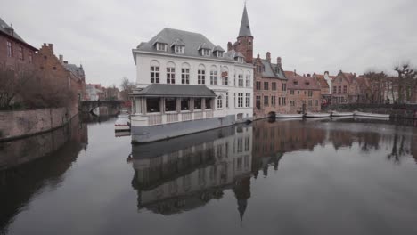 Duc-De-Bourgogne-Hotel-And-Restaurant-With-Specular-Reflection-In-Calm-Water-Of-Dijver-Canal-In-Bruges,-Belgium
