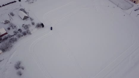 Bird's-Eye-View-on-Black-Car-Driving-Track-on-Snow-Covered-Field,-Tilt-Down