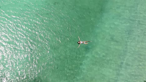 4k-aerial-drone-footage-of-a-lone-women-in-a-bikini-swimming-in-the-beautiful-clear-coastal-waves-of-a-resort-in-Ko-Larn-Island,-Thailand