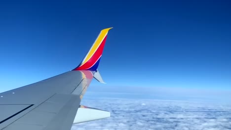 View-out-airplane-window,-Southwest-plane-wing-above-clouds-on-a-clear-day