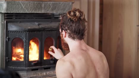 Caucasian-Man-Half-Naked-Placing-A-Piece-Of-Cut-Log-In-An-Antique-Wood-Fireplace-During-Winter-In-Trondheim,-Norway