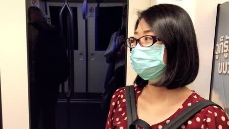 Thai-middle-aged-woman-wearing-a-medical-mask-while-standing-in-the-subway-train-or-MRT-of-Bangkok,-Thailand