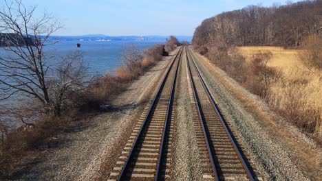 Aerial-drone-footage-down-railroad-train-tracks-in-a-river-valley-with-water-in-early-spring