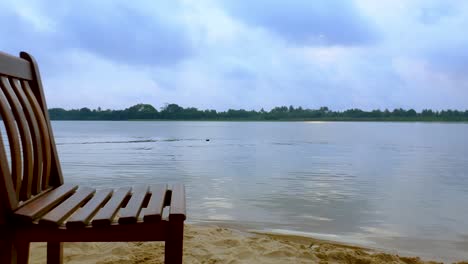 Vacant-wooden-chair-lying-along-the-silent-and-calm-river-on-cloudy-day