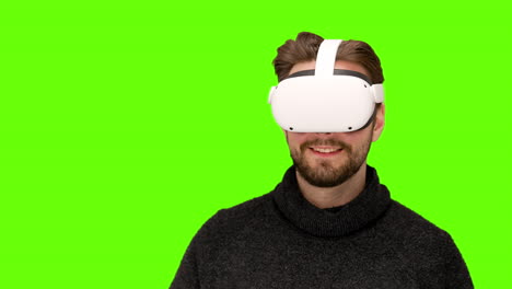 Close-up-of-man-in-latest-modern-white-oculus-quest-2-vr-ar-headset-playing-with-mixed-augmented-reality-controls-swiping-around-green-screen-chroma-keying-futuristic-communications-experience-happy