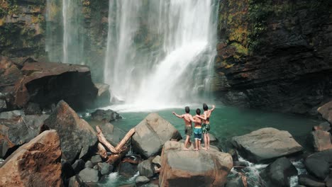 Three-men-on-rocks-with-arms-wide-open-in-front-of-Nauyaca-waterfall,-Costa-Rica