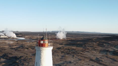 Red-and-white-lighthouse-tower-with-volcanic-landscape-in-background,-aerial
