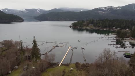Drone-shot-of-lake,-snowy-mountains-with-docks-in-Canada-Vancouver-Island