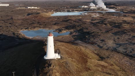 White-lighthouse-on-hill-surrounded-by-volcanic-landscape-and-geothermal-pools