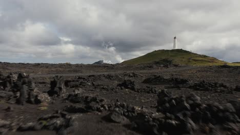 Low-aerial-over-rugged-volcanic-surface-with-Reykjanesviti-lighthouse-on-hill
