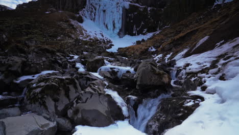 Ice-On-Cliff-With-Grundarfoss-Waterfall-Flowing-Into-The-Rocky-River-At-Winter-In-Iceland
