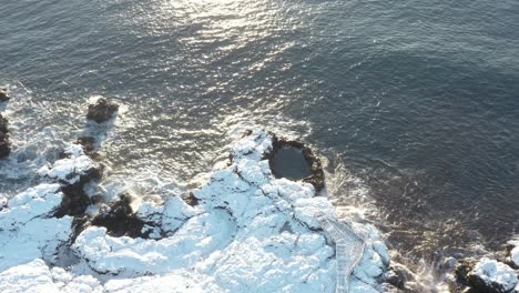 Scenic-rock-pool-on-wild-coast-of-Iceland-covered-in-white-snow-with-sunlight