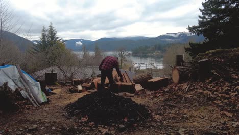 time-lapse-of-man-chopping-firewood-with-lake,-mountains-and-fast-moving-clouds