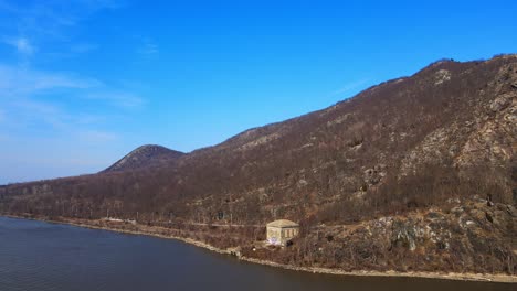 Aerial-drone-footage-pulling-away-from-a-mountain-and-over-a-river-in-new-york-state-in-the-hudson-valley-over-the-hudson-river-in-early-spring-by-breakneck-ridge