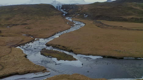 Curve-River-Running-Down-The-Fields-By-Svodufoss-Waterfall-With-Glacier-capped-Stratovolcano-Of-Snaefellsjokull-In-Background