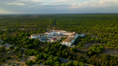 Aerial---Drone-Slowly-Approaching-to-Luxury-Garden-Playanatural-Hotel-Surrounded-with-Dense-Evergreen-Stone-Pine-Tree-Forest-at-Sunset,-El-Rompido,-Andalusia-skyline,-Spain