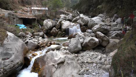 Ein-Kleiner-Fluss,-Der-In-Den-Ausläufern-Des-Himalaya-Fließt,-Mit-Kleinen-Steinhütten-Daneben