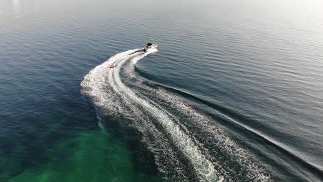 Following-aerial-tracks-child-tubing-behind-powerboat-in-clear-water